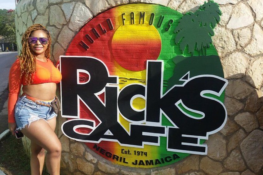 A person standing in front of a sign for Rick's Cafe, which is labeled as a world-famous establishment in Negril, Jamaica, established in 1974. 4