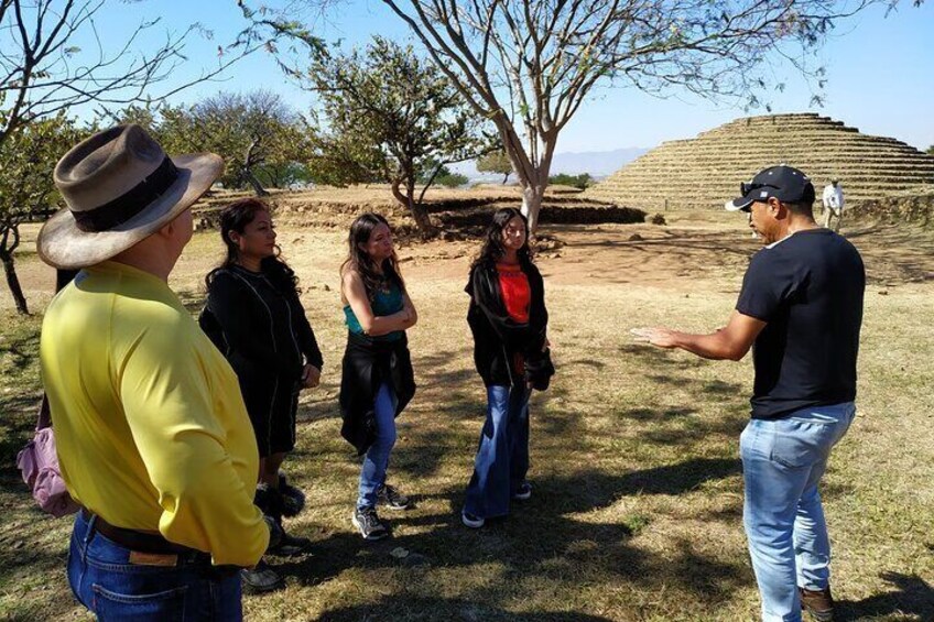 A group of people standing outdoors, a tree, and a mound in the background. 5