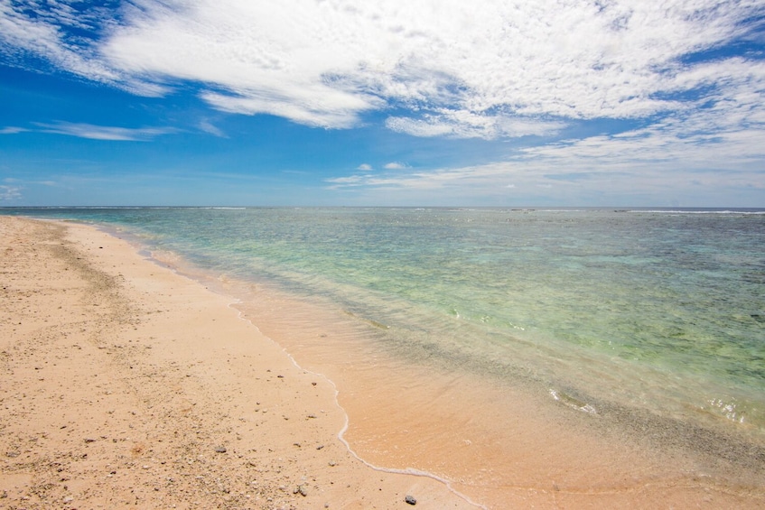 A sandy beach with clear turquoise water and a partly cloudy sky. 5