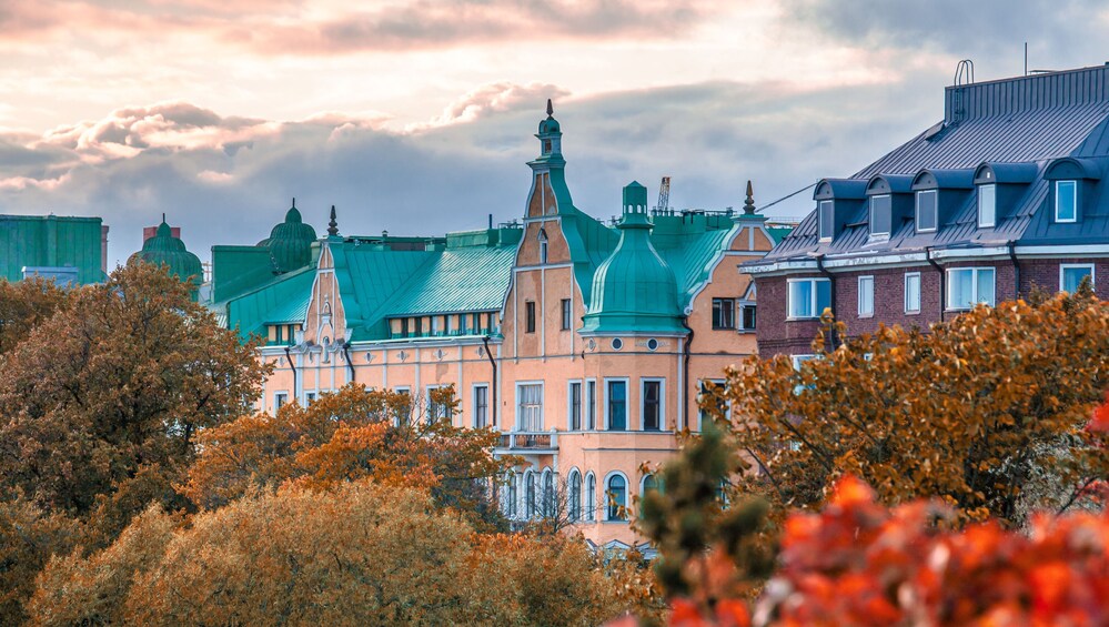 A historic building with green roofs and a pink facade, surrounded by autumn foliage. 2
