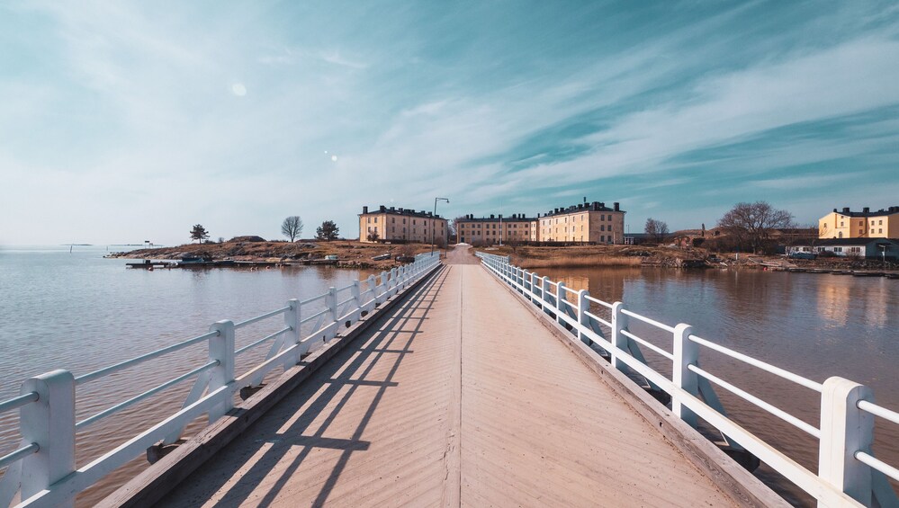 A wooden boardwalk leading to buildings by a calm river. 5