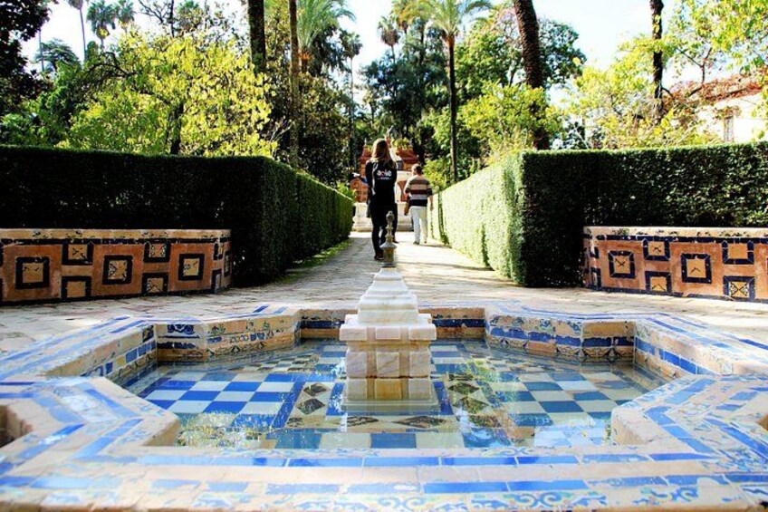 A tiled fountain with geometric patterns, surrounded by neatly trimmed hedges and a pathway. 2