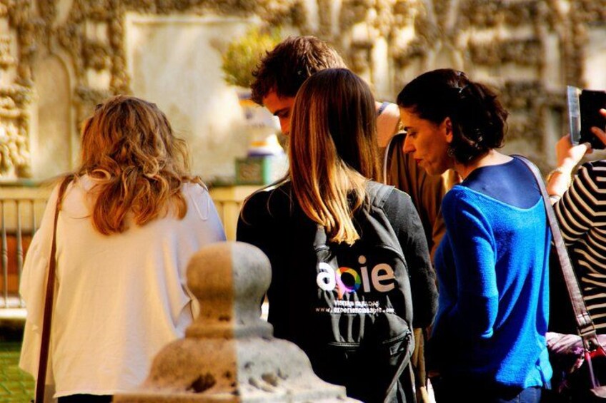 A group of people standing outdoors, possibly at a historical site with stone structures and greenery in the background. 4