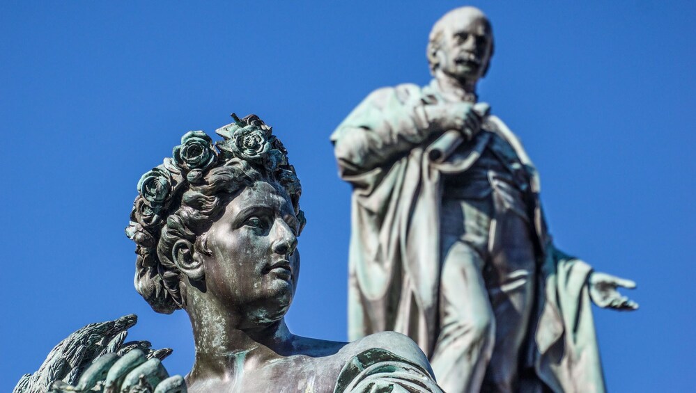 Une statue représentant une femme coiffée d’une couronne de fleurs et un homme vêtu d’une robe. 1