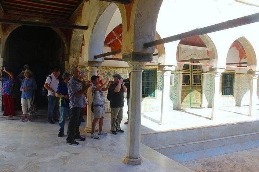 Un groupe de personnes se tient dans une cour intérieure ornée d’arcades et dont le sol est recouvert de carreaux. 5
