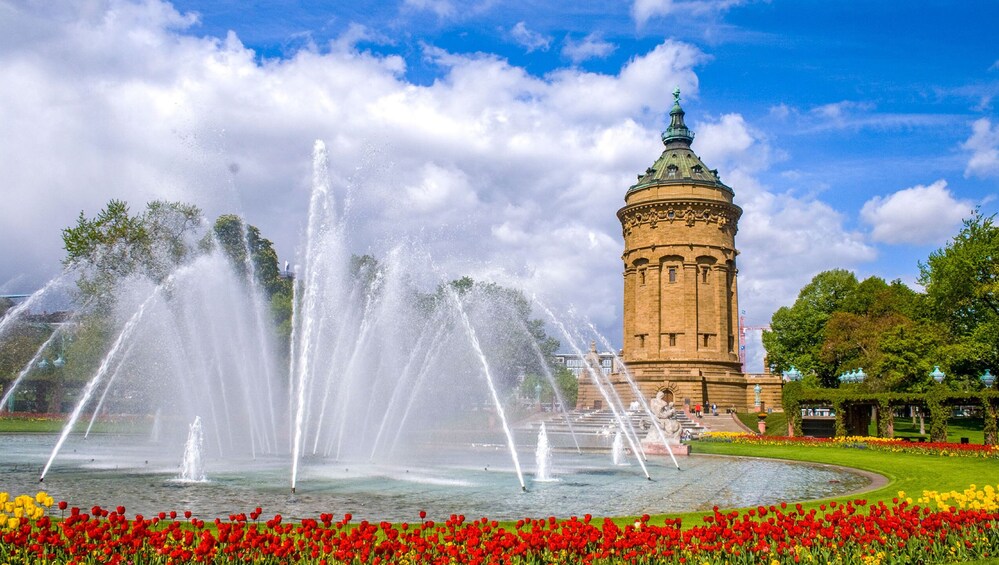 A historic tower with a clock, surrounded by a fountain and colorful tulips. 4