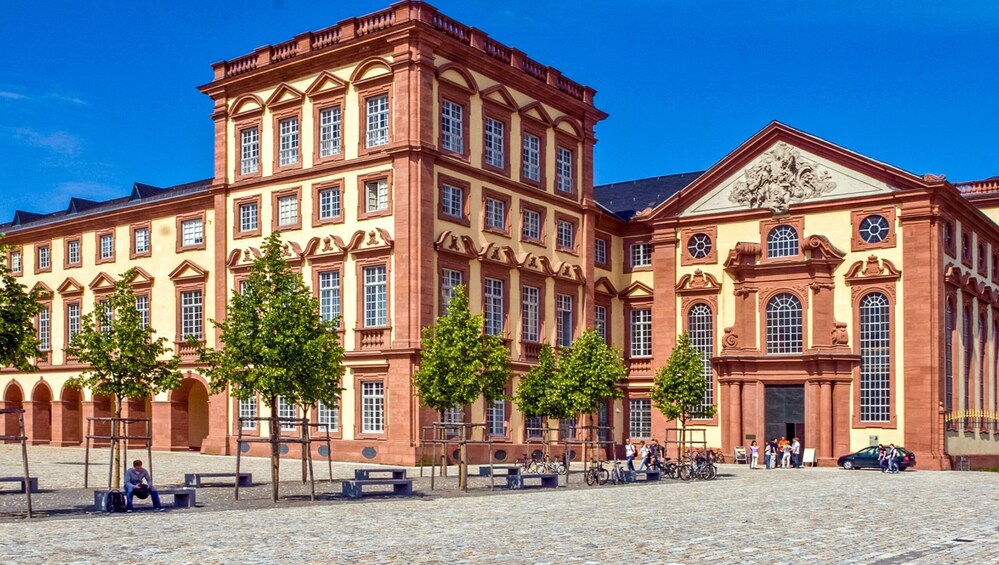 A historic building with red brick architecture, large windows, and a central entrance with a decorative pediment. 1