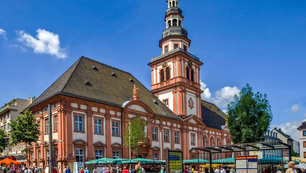 A historic building with a clock tower, surrounded by market stalls and pedestrians. 2