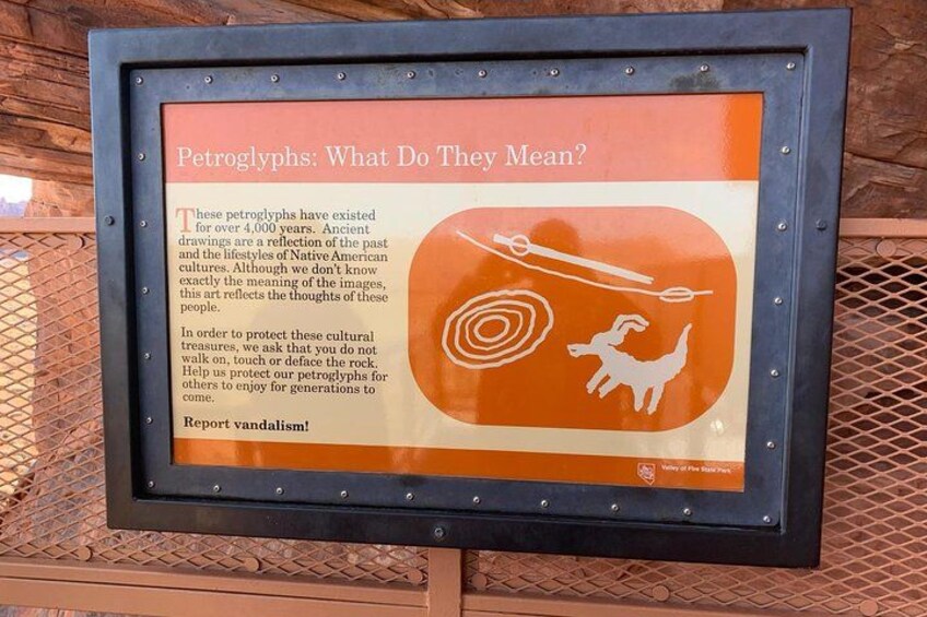 A framed informational sign about petroglyphs, featuring a drawing of a human figure and a bison. 3