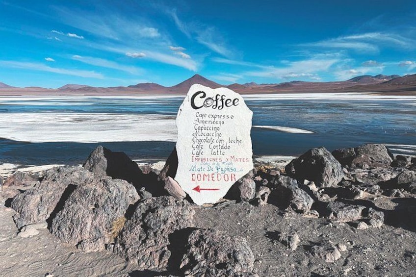 Ein Schild mit der Aufzählung verschiedener Kaffeesorten vor einer abgelegenen, felsigen Landschaft mit See und Bergen im Hintergrund. 2