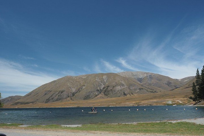 A lake with mountains in the background, a clear sky, and a person fishing. 3