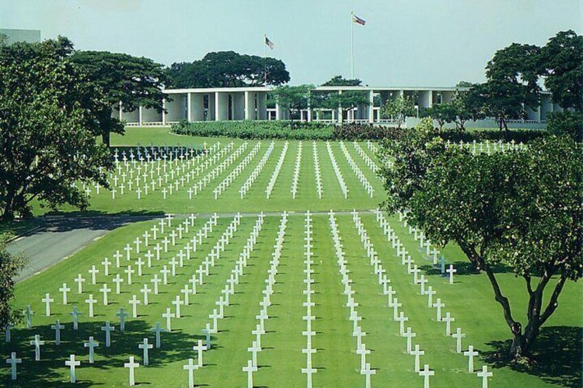 Un cementerio con hileras de cruces blancas, un edificio al fondo y una bandera ondeando. 2