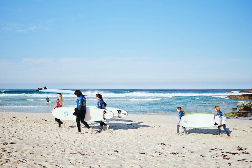 A leisurely walk with a view. Stroll along the stunning Redgate Beach with surfboards in hand, embracing the beauty of nature.