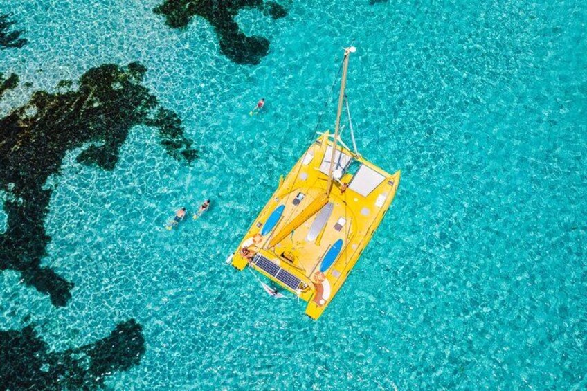Un bote amarillo flota sobre aguas turquesas cristalinas, con gente nadando alrededor. 2