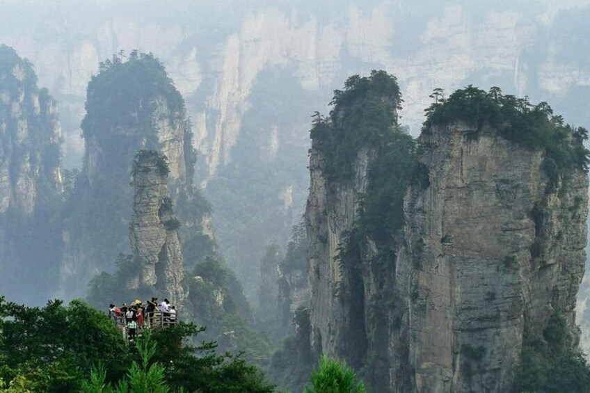 Un gruppo di persone su una piattaforma panoramica che domina formazioni rocciose alte e strette, coperte da vegetazione lussureggiante. 1