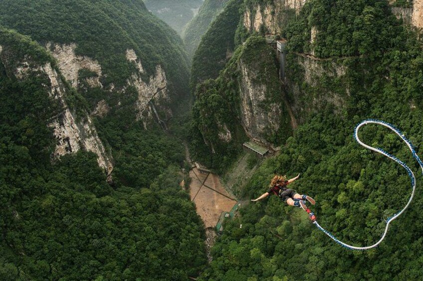 A person bungee jumping from a high cliff with a rope, surrounded by dense forest and steep cliffs. 1