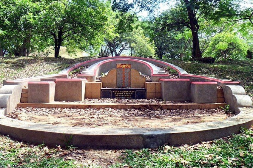 A memorial with a curved roof and inscriptions, surrounded by a circular concrete base and greenery. 2