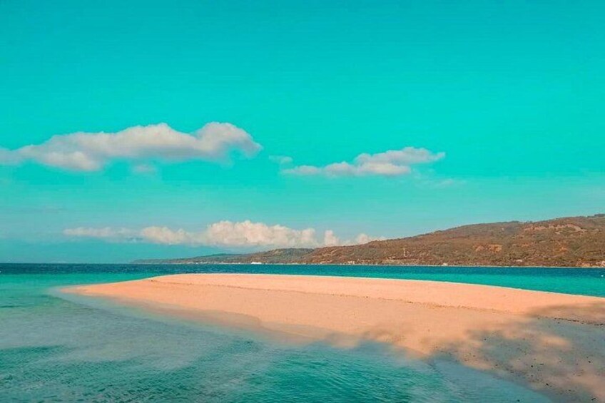 A beach with clear turquoise water, a sandy shore, and distant hills. 1