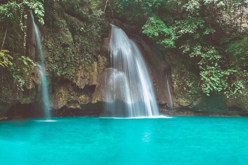 A waterfall cascading into a turquoise pool surrounded by lush greenery. 5