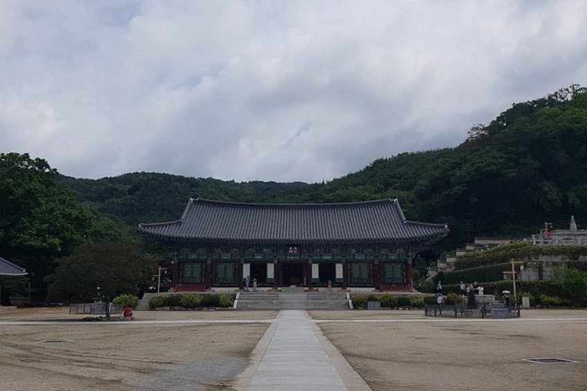 A traditional Korean building with a tiled roof, surrounded by a paved area and a forested hill. 4