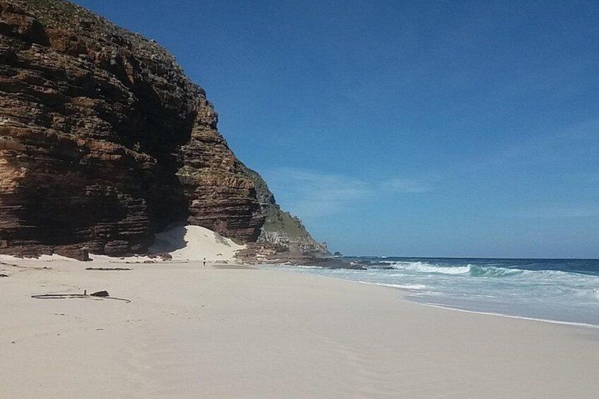 Una spiaggia con sabbia bianca, una scogliera rocciosa e onde che si infrangono sulla riva. 3