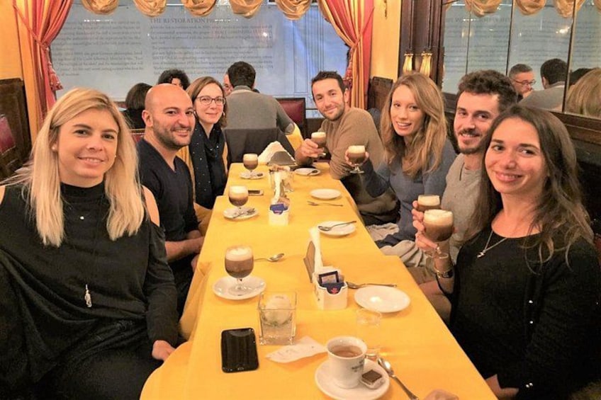 En gruppe mennesker sidder ved et langt bord i en restaurant med flere retter og drikkevarer. 1