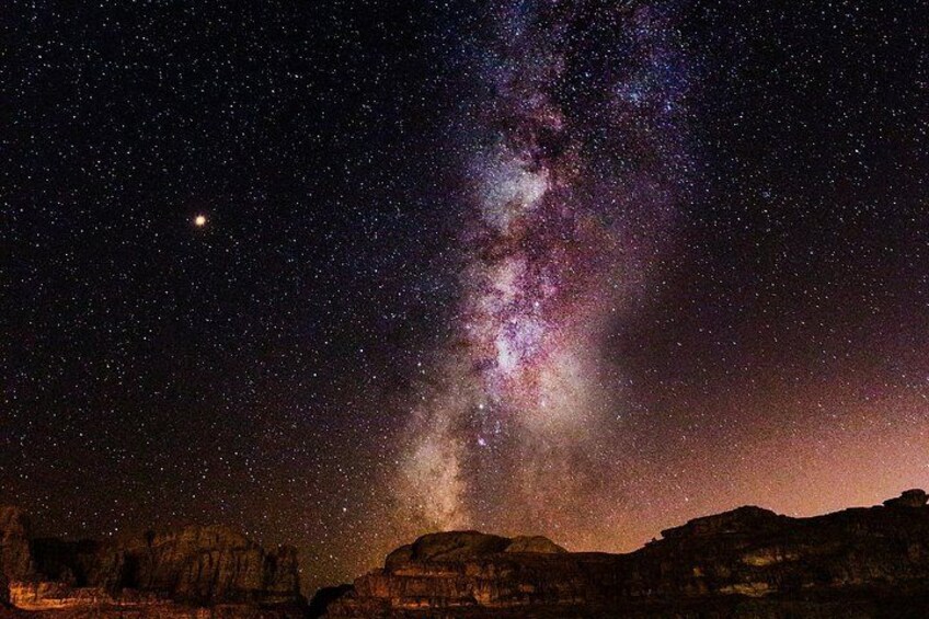 Un ciel nocturne étoilé où l’on aperçoit la Voie lactée, une chaîne de montagnes se détachant en silhouette, et une petite planète dans le coin supérieur gauche. 3