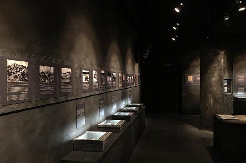 Un couloir de musée faiblement éclairé, avec des vitrines et des panneaux d’information fixés aux murs. 1