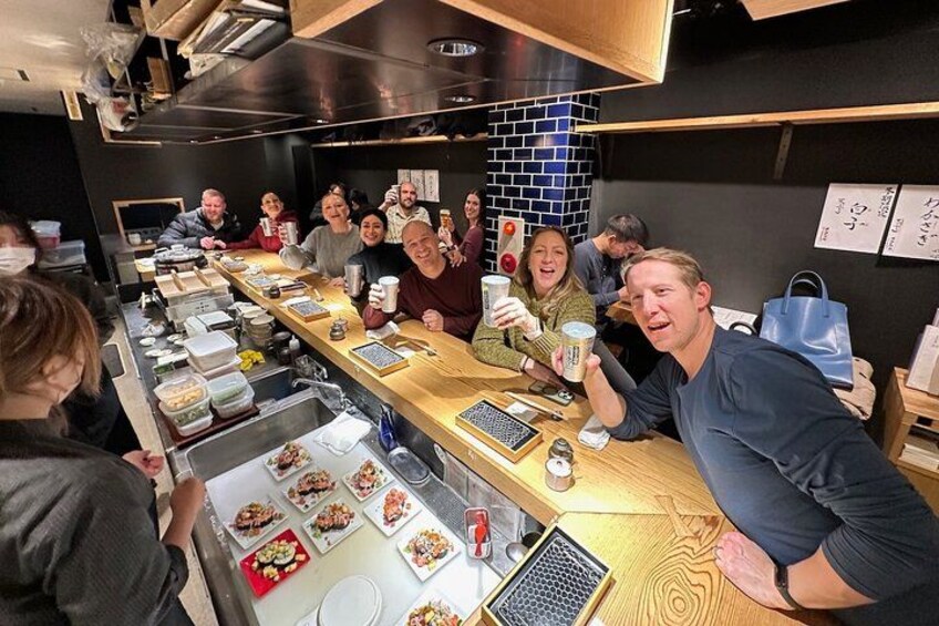 Un grupo de personas sentadas en una larga mesa de madera en un restaurante, con comida y bebidas sobre la mesa. 2