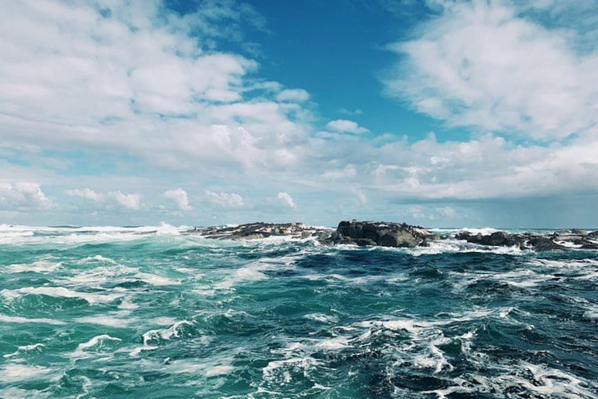 Een onstuimige zee met golven die tegen rotsformaties slaan, onder een gedeeltelijk bewolkte lucht. 4