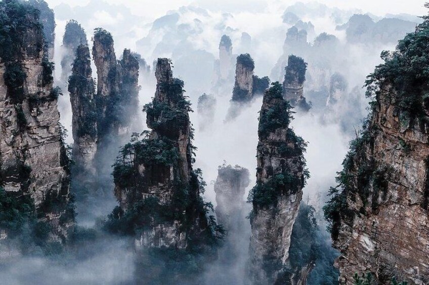 Towering limestone peaks with dense vegetation, surrounded by mist. 1