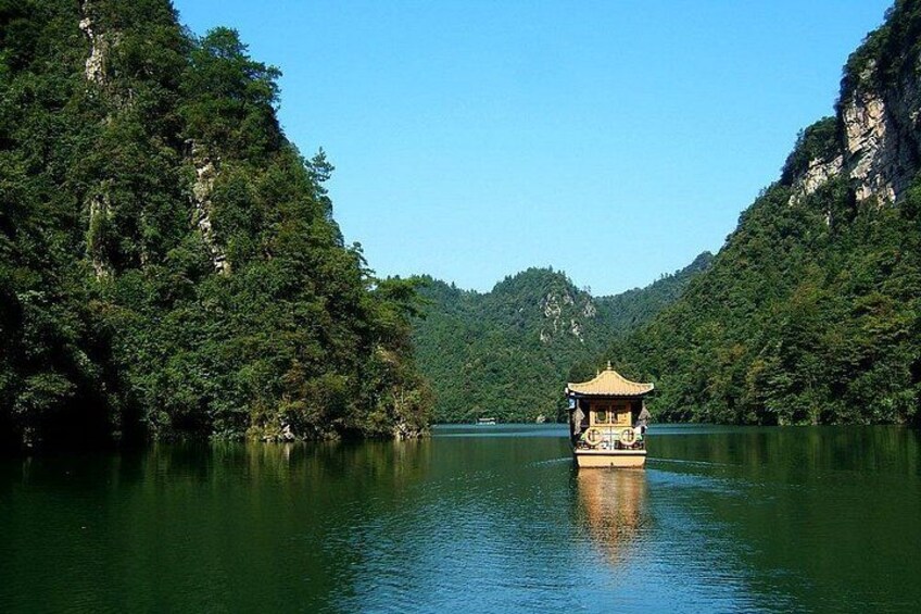 A traditional boat with a pagoda-style roof on a calm river surrounded by dense forest and cliffs. 1