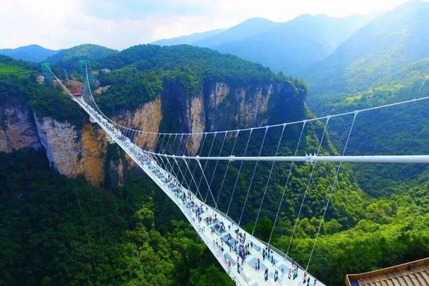 A suspension bridge with people walking across it, surrounded by lush green mountains. 4