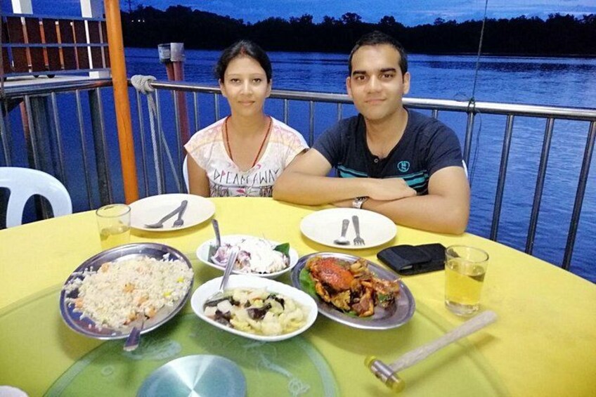 Dos personas sentadas a una mesa con varios platos, incluyendo arroz y mariscos, en un barco con un lago al fondo. 4