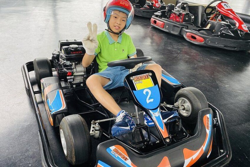 A child in a go-kart with the number 2, wearing a helmet and a green shirt. 4