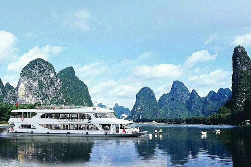 A river cruise boat on calm waters with limestone karst formations in the background. 1