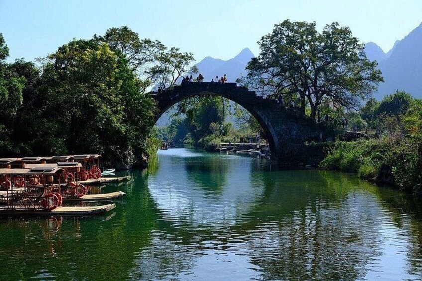Un fiume con un ponte di pietra, imbarcazioni e vegetazione rigogliosa. 3