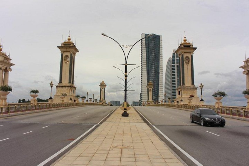 A bridge with two clock towers, a modern building, and a car on the road. 5