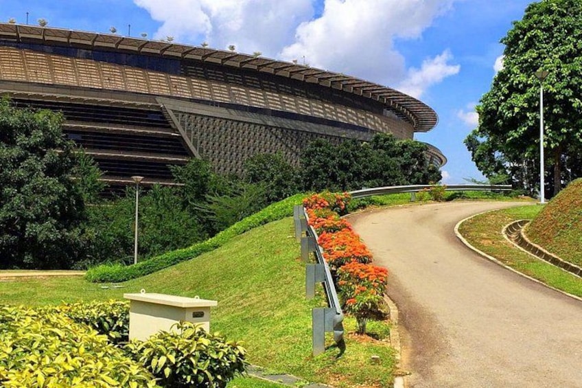 A stadium with a curved roof, surrounded by greenery and a curved road. 4