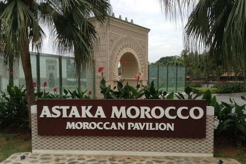 A sign for Astaka Morocco Pavilion with an ornate archway and tropical plants. 3