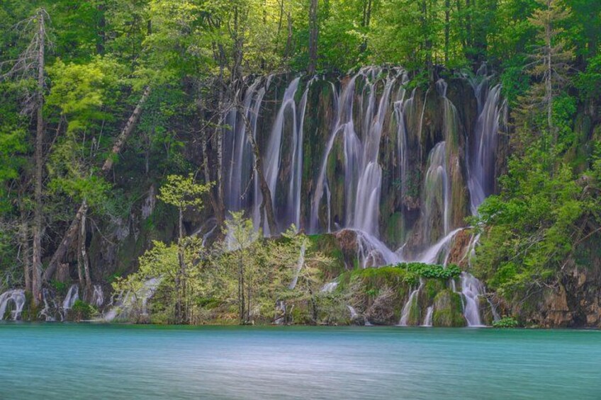 A waterfall cascading into a turquoise lake surrounded by dense green forest. 4