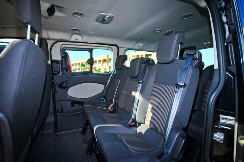 A vehicle interior with black seats, a central console, and a window view of buildings. 5