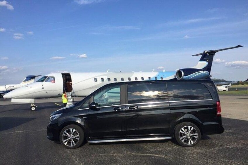 A black van parked on a tarmac with a private jet in the background. 1