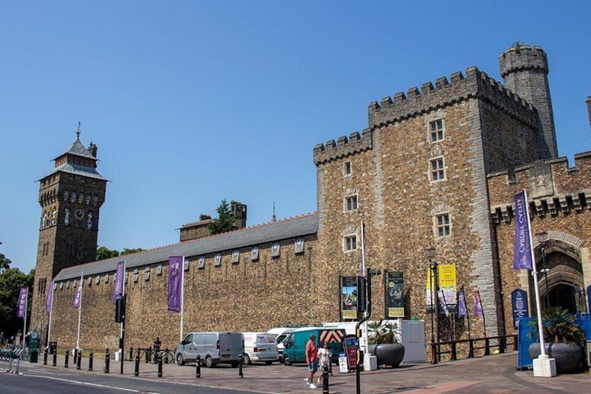 A historic building with a clock tower, banners, and a paved street with vehicles and pedestrians. 2