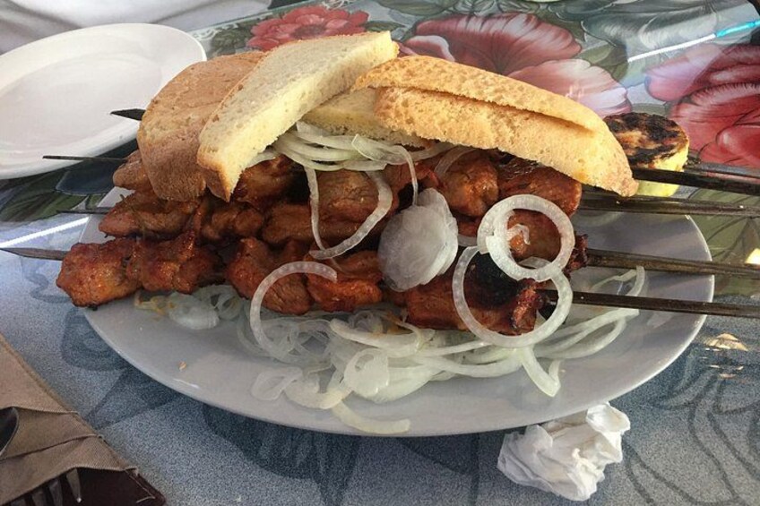 Une assiette de viande grillée en brochettes, accompagnée d’oignons, et un sandwich. 5