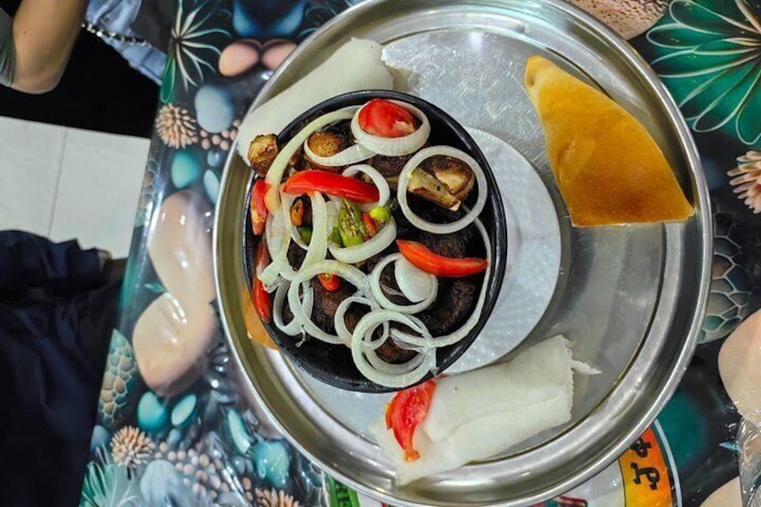 A meal with a black bowl containing sliced vegetables and a white dish with a red sauce, served on a metal plate. 2
