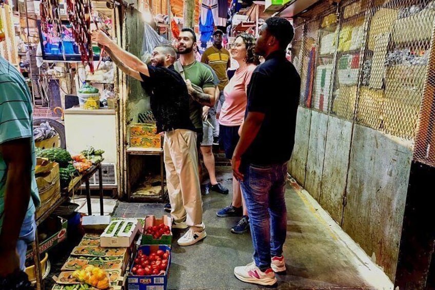 A narrow market alley with people browsing stalls selling fruits and vegetables. 5