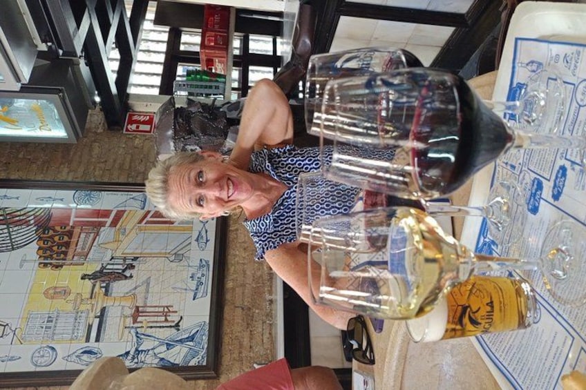 A person seated at a table with a large glass of wine, a menu, and a decorative wall with architectural drawings. 3