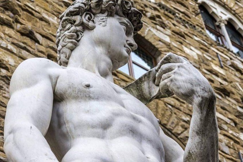 A classical statue with intricate hair details and a muscular build, set against a stone wall background. 4