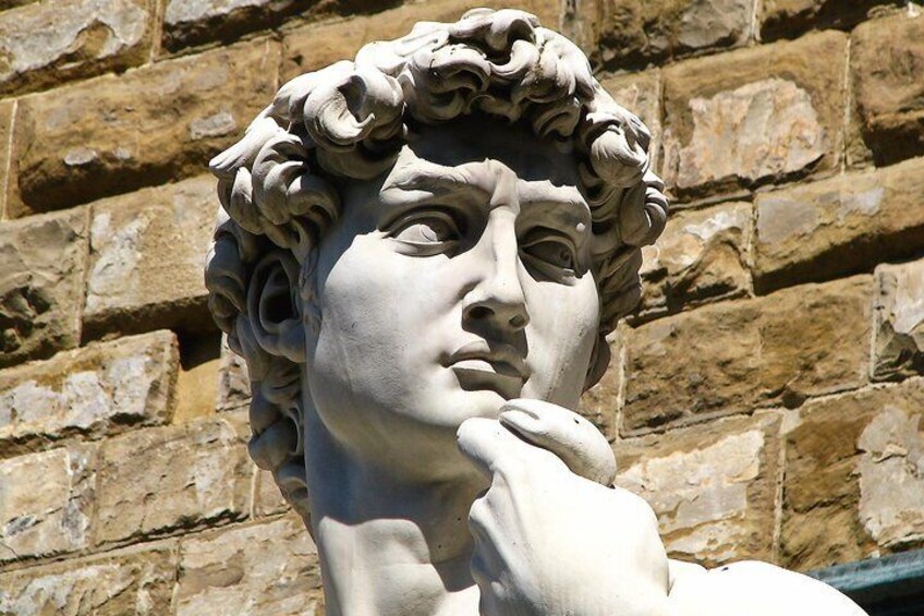 Scultura in pietra raffigurante una figura con capelli ricci, su sfondo di un muro in pietra. 2